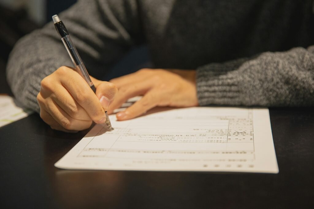 Crop anonymous male in gray sweater writing in form of important document at table